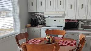 Un coin repas avec une table et des chaises en bois, des meubles blancs et une fenêtre avec des stores.