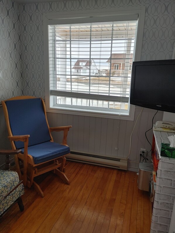 A room with a wooden rocking chair, a television, and a window with blinds.