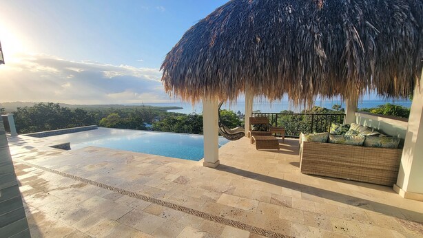 A poolside area with a thatched roof, wicker furniture, and a view of the sea. - Sweeping panoramic views of the reef  (Bay Islands Department)