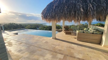 A poolside area with a thatched roof, wicker furniture, and a view of the sea.
