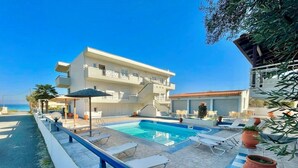 Un área de piscina con sillones reclinables, una piscina pequeña y un edificio con balcones.