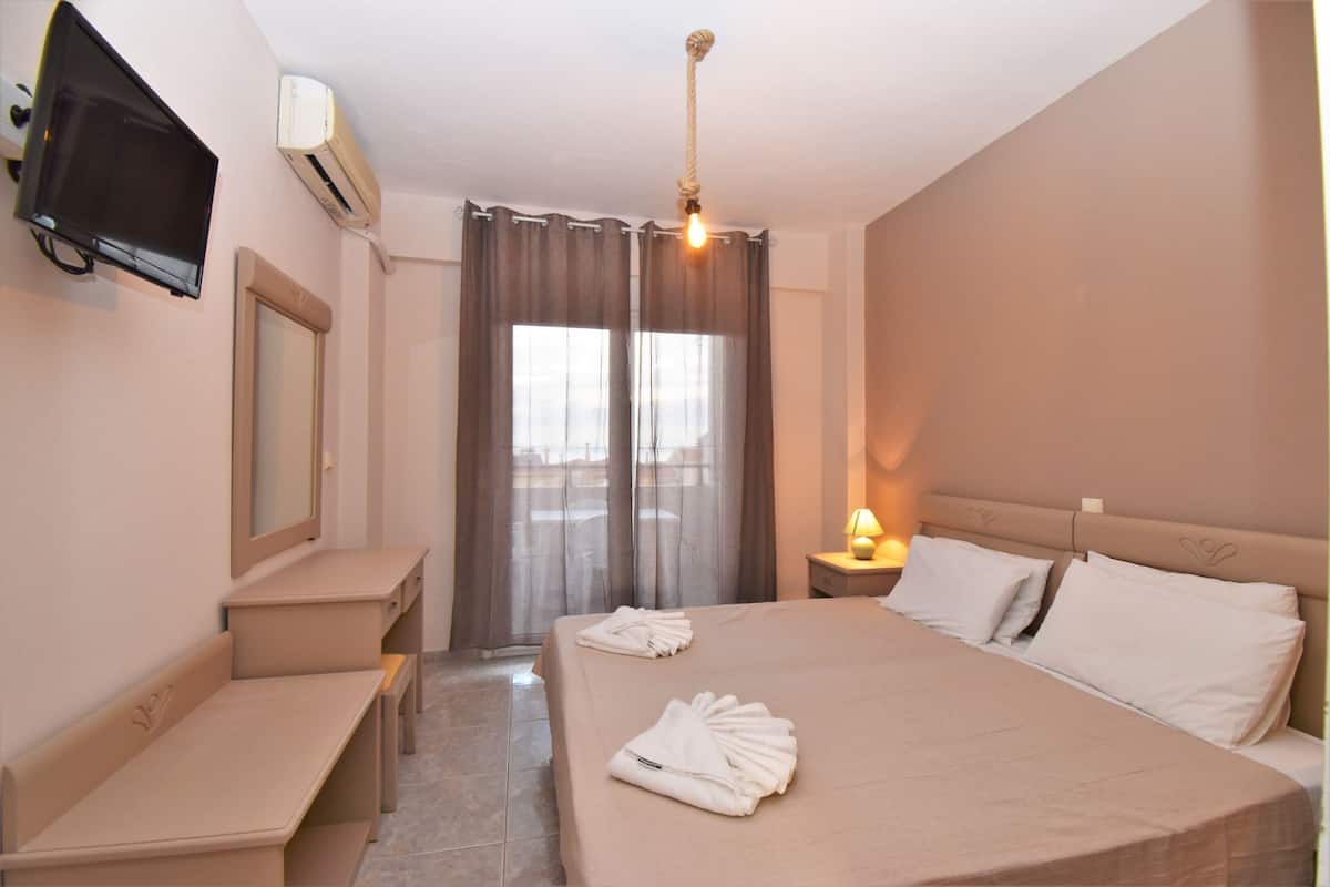 Hotellihuone, jossa on sänky, työpöytä, tuoli, televisio ja ikkuna, jossa on verhot.
