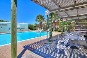 A poolside area with a wooden deck, lounge chairs, and a table.