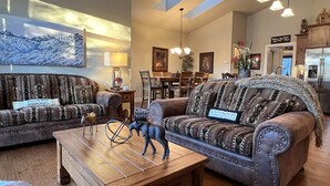 Un salón espacioso con dos sofás estampados, una mesa de centro de madera y un comedor con una araña.