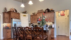 Una cocina con armarios de madera, una isla central con sillas, un refrigerador y diversos objetos decorativos.