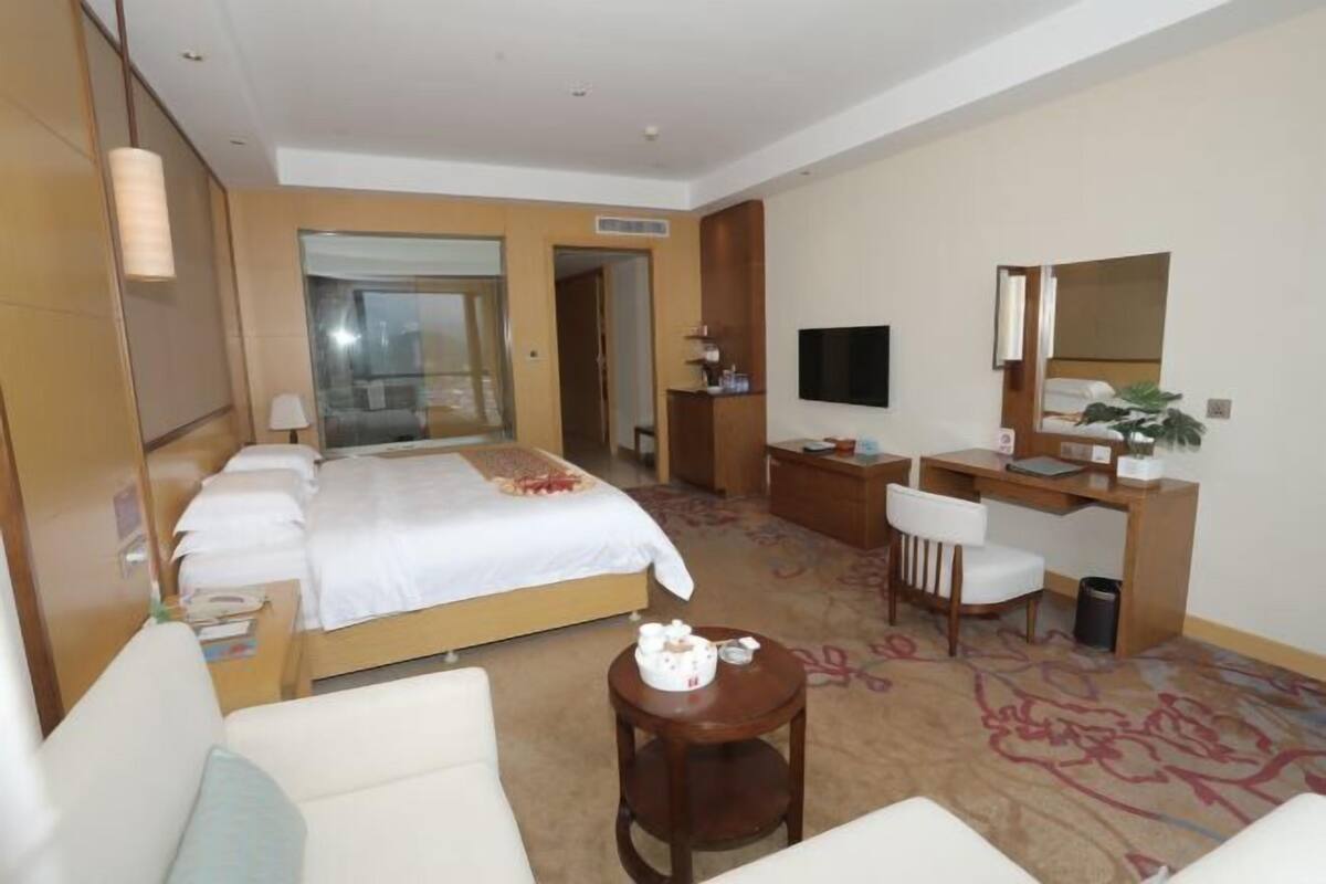 A hotel room with a bed, a desk, a chair, a TV, and a small table with a decorative item.