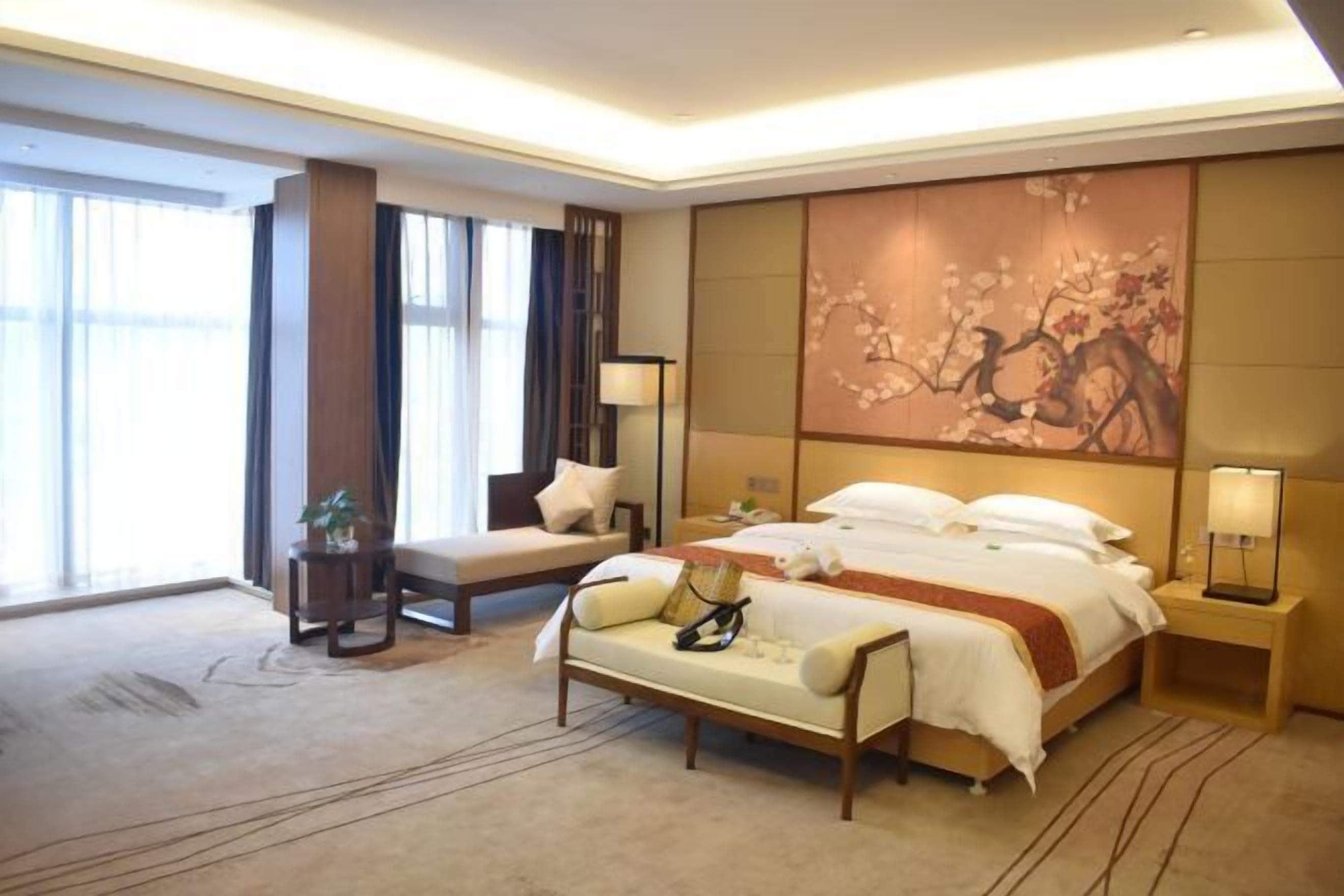 Ein modernes Hotelzimmer mit einem großen Bett, einer Couch, einem Nachttisch und einem großen Fenster.