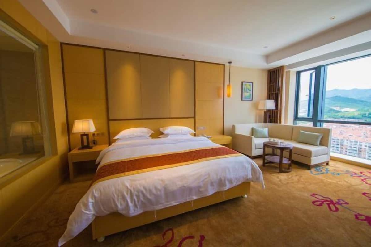 A hotel room with a large bed, a sofa, a small table, and a view of the mountains.