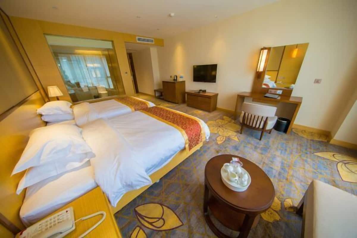 A hotel room with a large bed, a desk, a chair, a telephone, and a television.