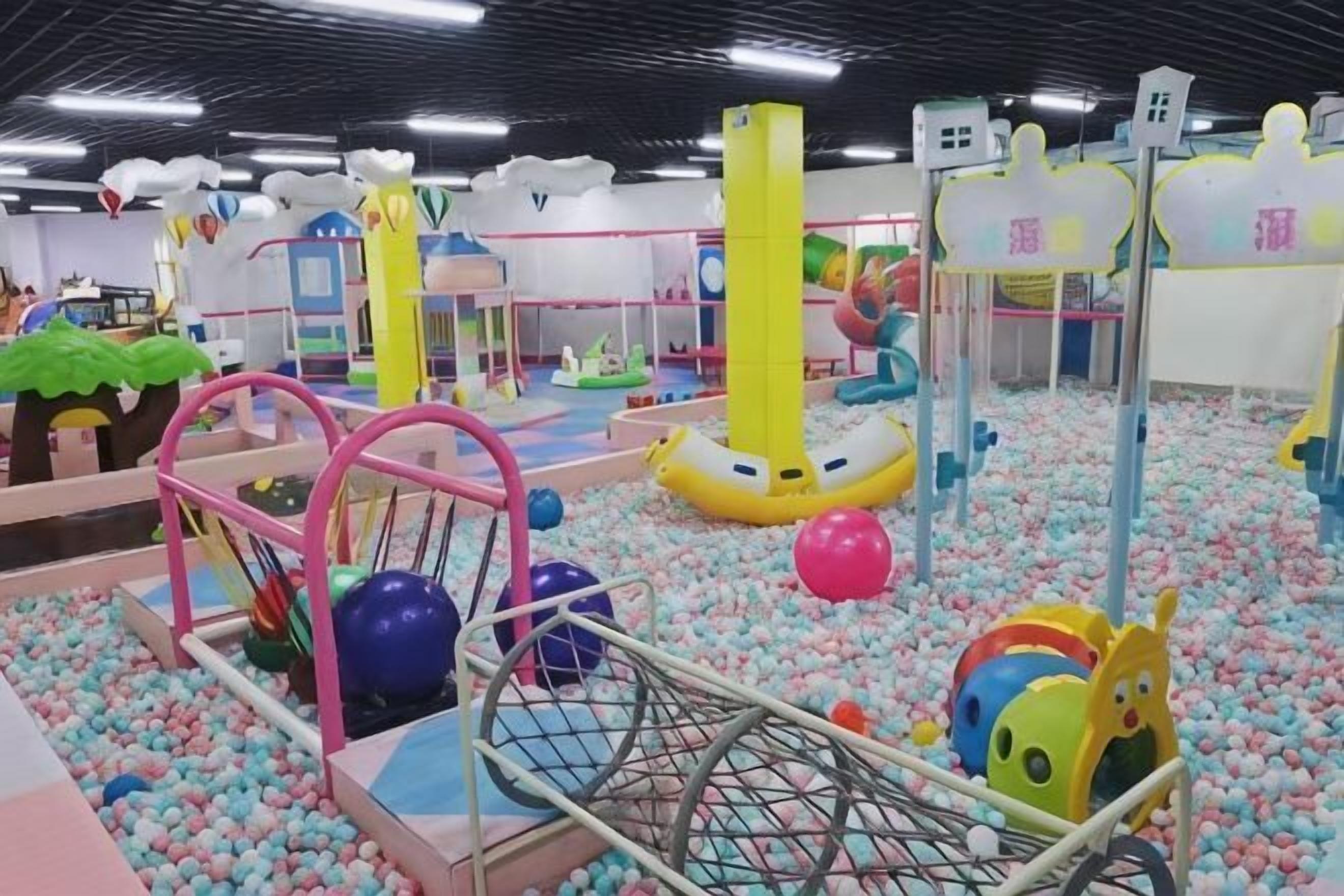 Un área de juegos infantiles con diversas estructuras, una piscina de pelotas y superficies acolchadas.