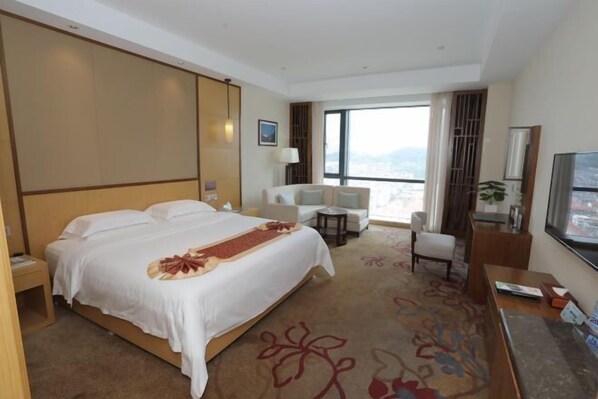A hotel room with a large bed, a desk, a chair, a TV, and a view of the city. - Wen Gong Hotel (Youxi)