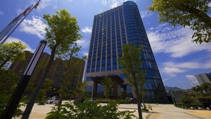 A modern high-rise building with a glass facade, surrounded by greenery and other buildings. - Wen Gong Hotel (Youxi)