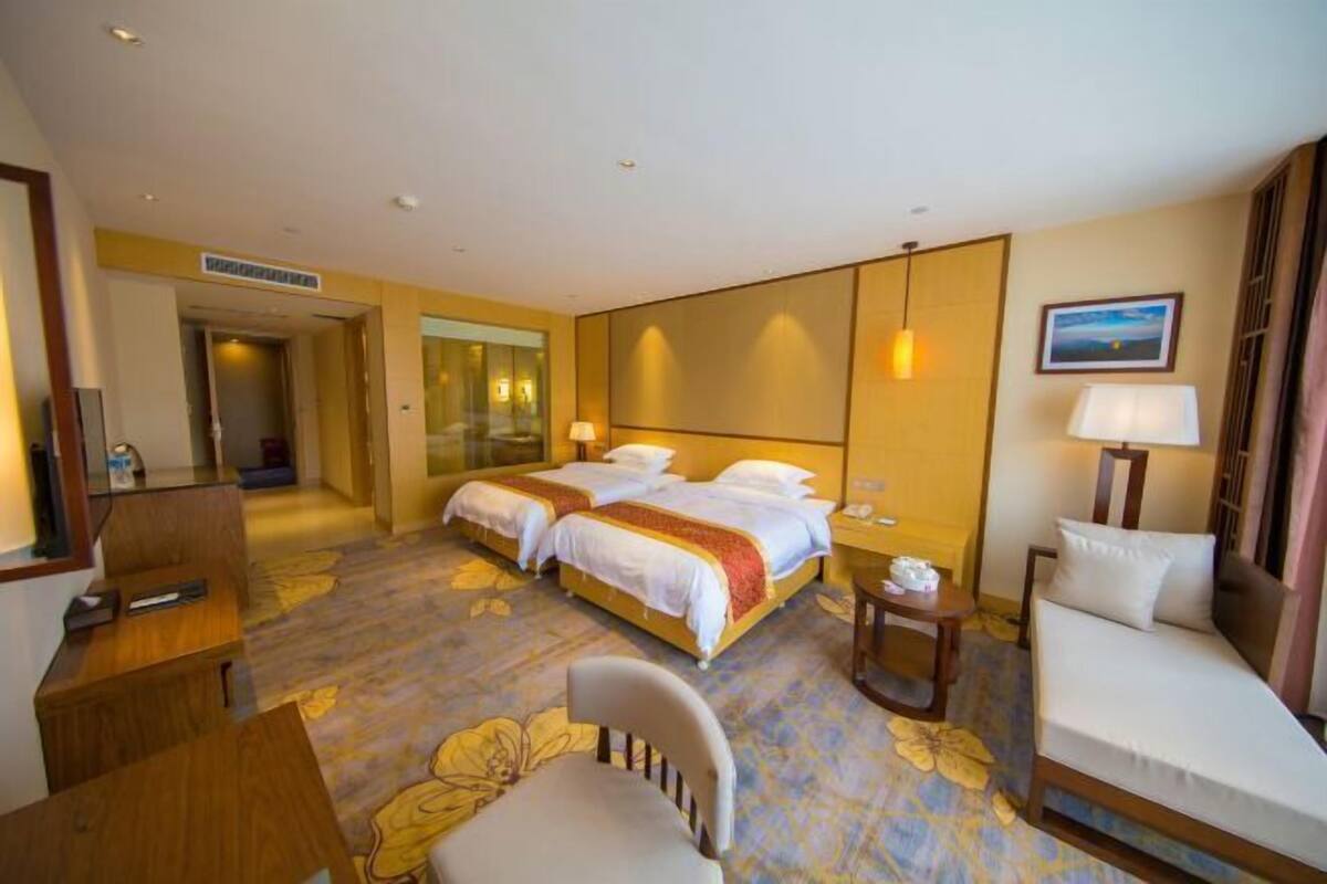 A hotel room with two beds, a sofa, a chair, a desk, and a small table.