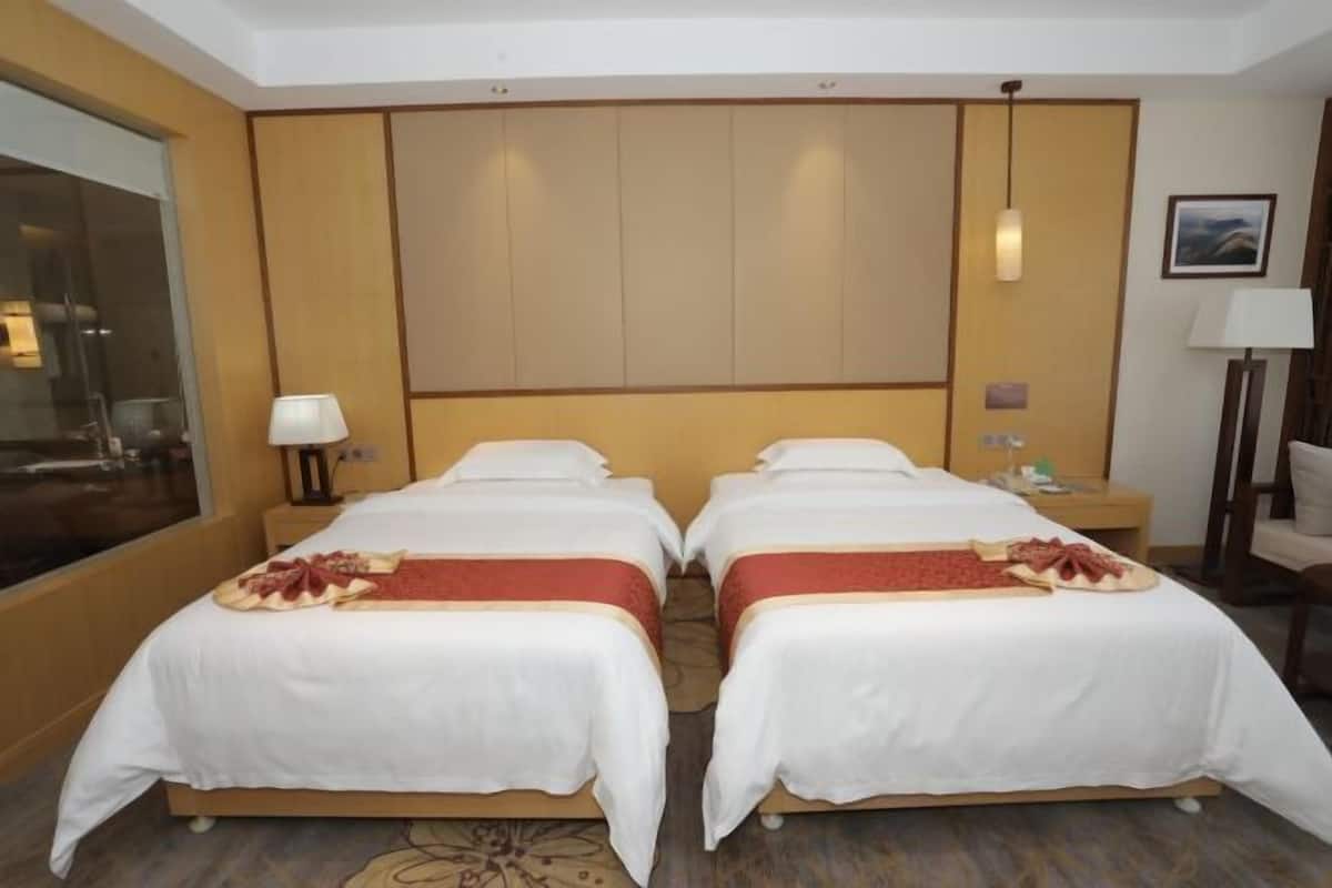 A hotel room with two beds, a large window, a wooden headboard, and a nightstand with a lamp.