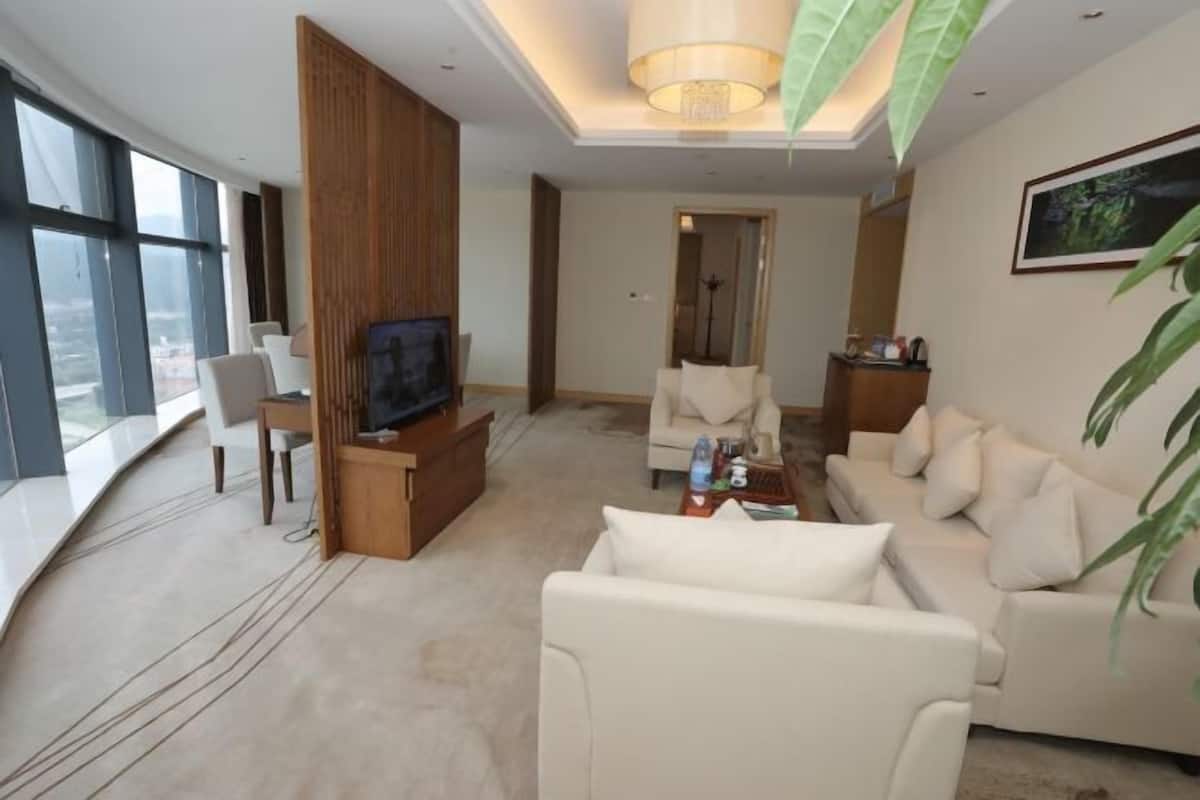 A modern living room with a flat-screen TV, a sofa, a coffee table, and a large window offering a city view.
