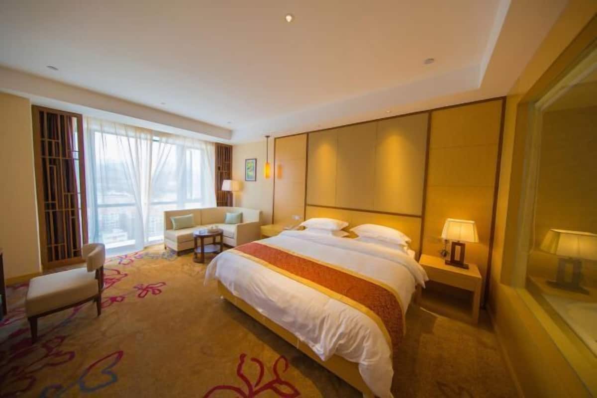 A hotel room with a large bed, a sitting area with a sofa and armchair, a small table, and a window with curtains.