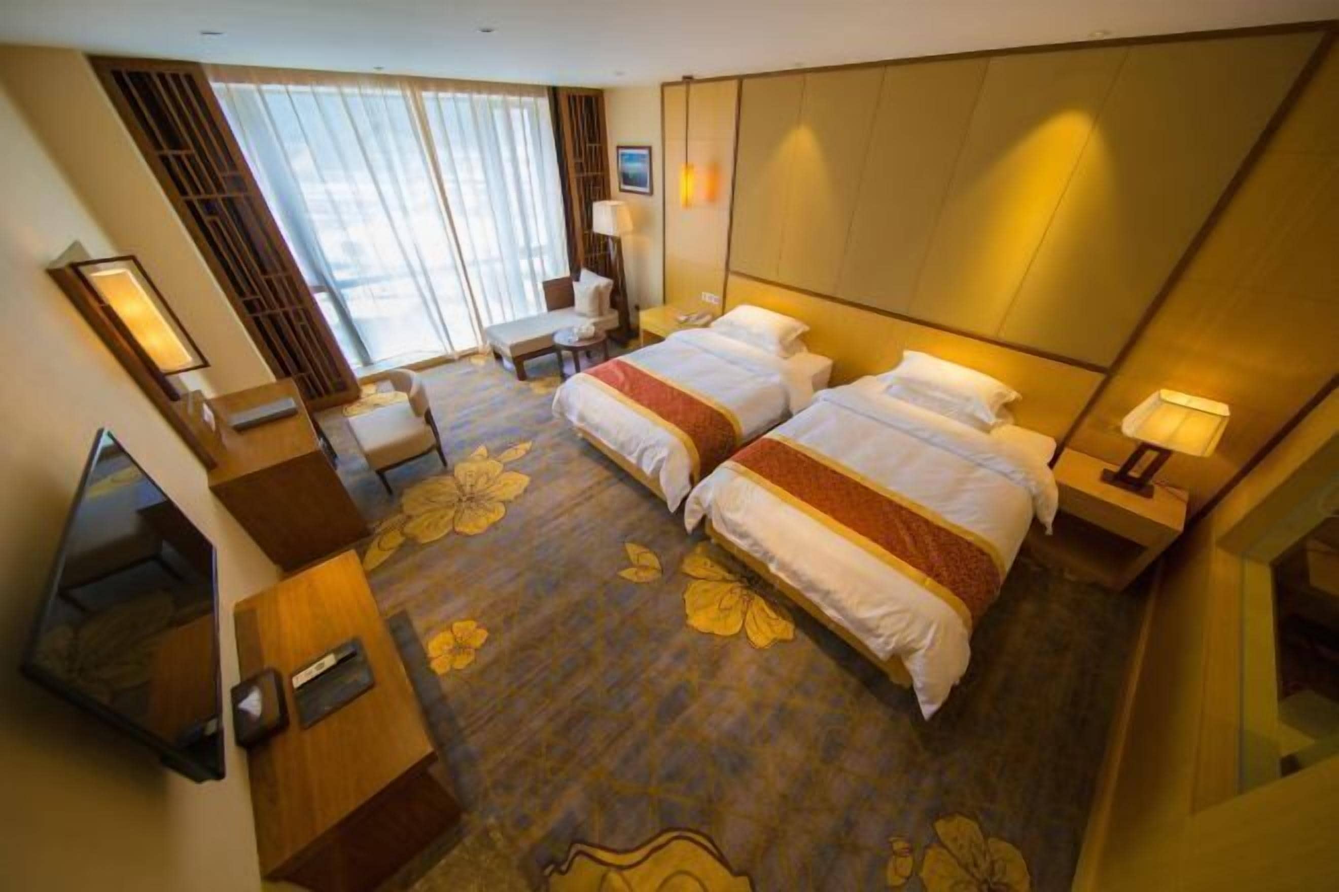 Habitació d'hotel amb dos llits, un escriptori, una cadira, una taula petita, un mirall i una finestra amb cortines.