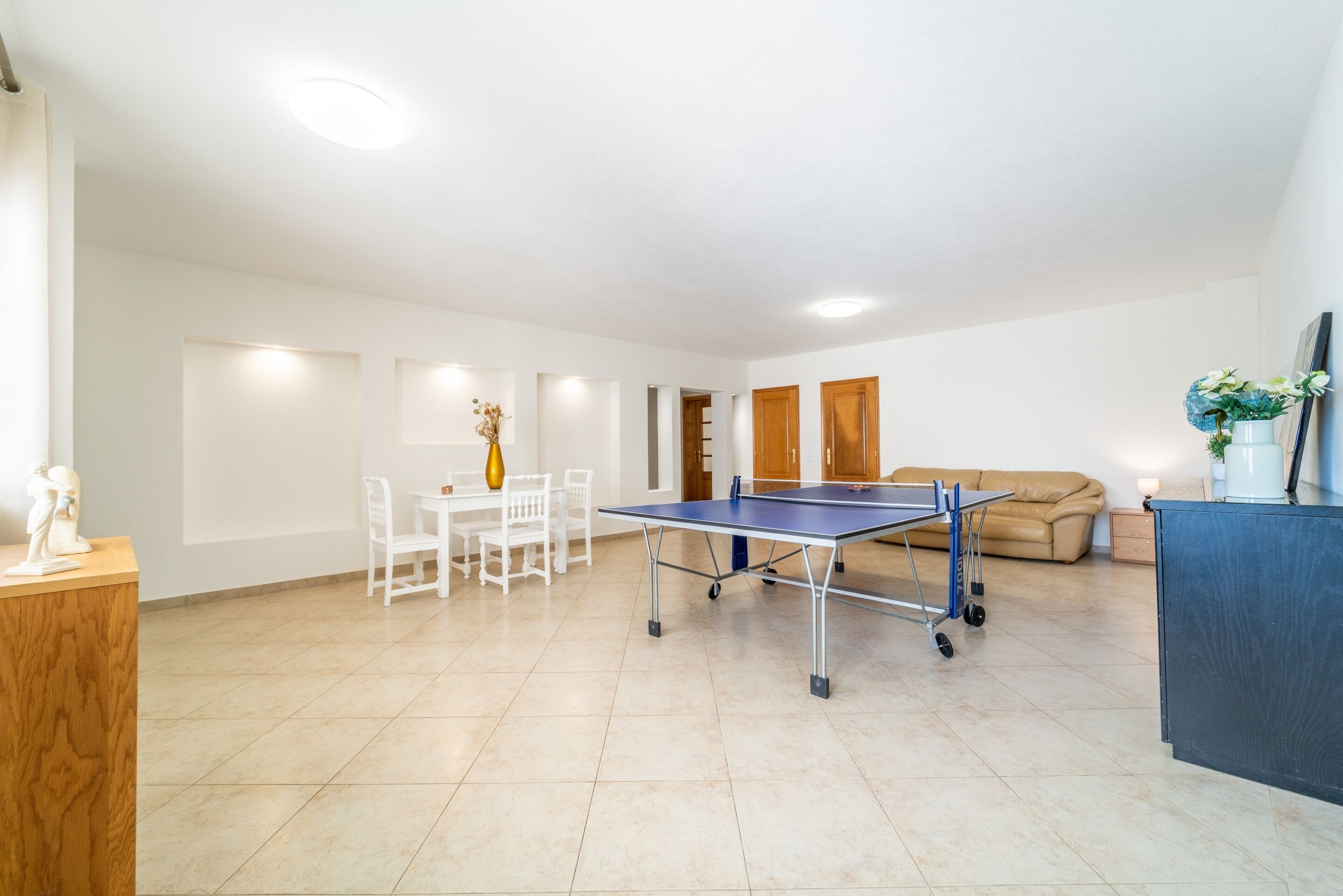 A spacious living area with a ping pong table, a sofa, and a dining table with chairs.