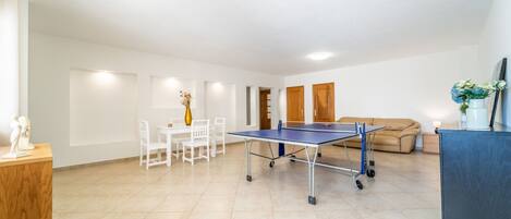 A spacious living area with a ping pong table, a sofa, and a dining table with chairs.
