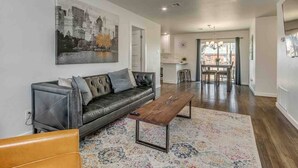 A modern living room with a black leather sofa, a wooden coffee table, and a colorful rug. - Luxury Modern 3BR - Private Primary Suite! (Oklahoma City)