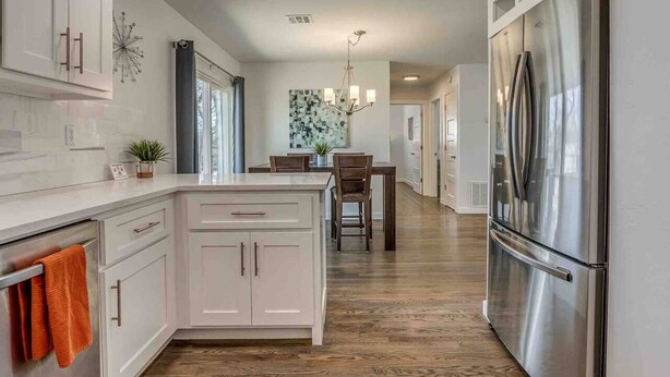 A modern kitchen with white cabinetry, a stainless steel refrigerator, and a wooden floor. - Luxury Modern 3BR - Private Primary Suite! (Oklahoma City)