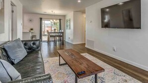 A living room with a leather sofa, a wooden coffee table, and a flat-screen TV mounted on the wall. - Luxury Modern 3BR - Private Primary Suite! (Oklahoma City)