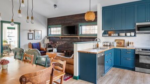 A modern kitchen with blue cabinets, a wooden dining table, and a TV mounted above the fireplace.