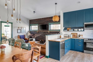 A modern kitchen with blue cabinets, a wooden dining table, and a TV mounted above the fireplace.