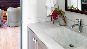 A modern bathroom with a marble sink, a large mirror, and framed artwork on the wall.
