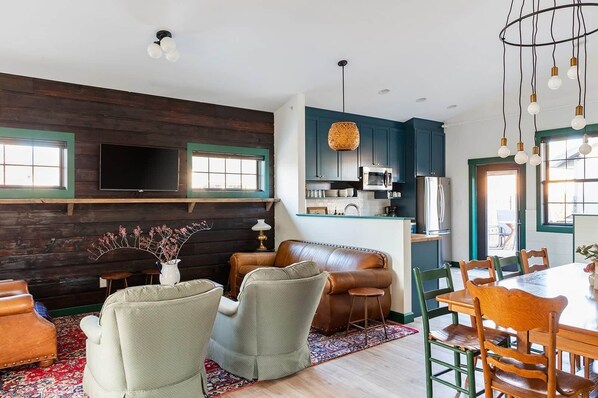 A modern kitchen with dark cabinetry, a flat-screen TV, and a dining area with a wooden table and chairs.