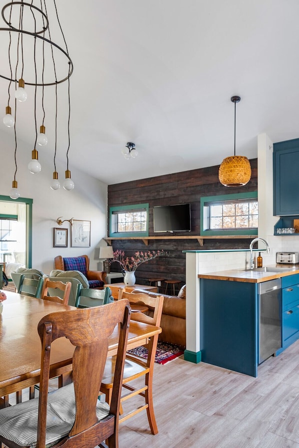 A modern kitchen with blue cabinets, a wooden dining table, and a hanging light fixture.