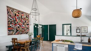 A modern kitchen with a wooden dining table, chairs, and a large abstract painting on the wall.