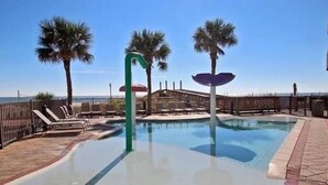 A swimming pool with palm trees, lounge chairs, and a fence. - Updated Beachfront Condo w/private balcony and Pool (Gulf Shores)