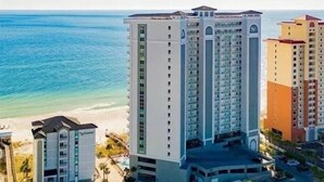 A high-rise hotel with multiple floors, a beach view, and a parking area. - Updated Beachfront Condo w/private balcony and Pool (Gulf Shores)