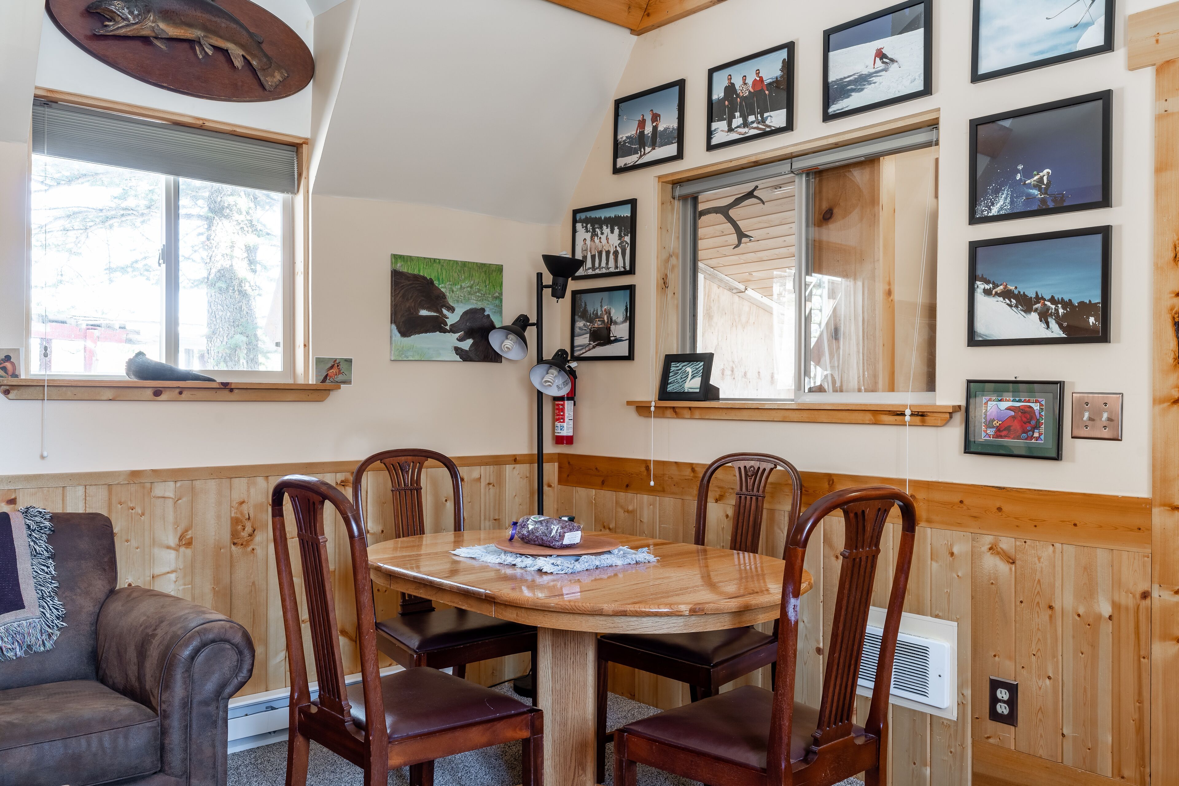 A dining area with a wooden table and chairs, surrounded by wooden paneled walls and framed pictures.