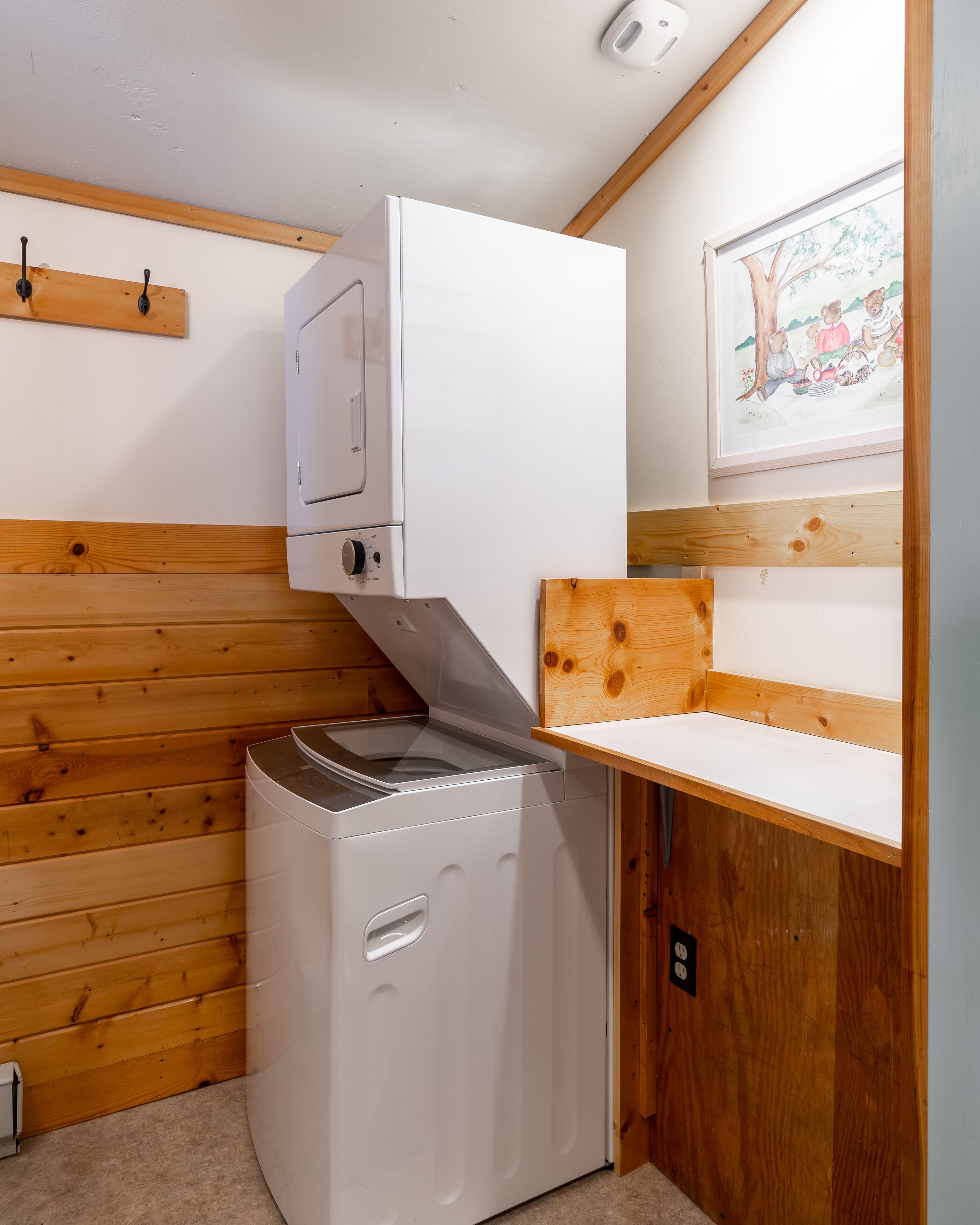 A compact kitchen with a white washing machine, wooden paneling, and a framed illustration on the wall.