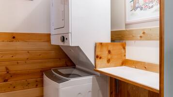 A compact kitchen with a white washing machine, wooden paneling, and a framed illustration on the wall.