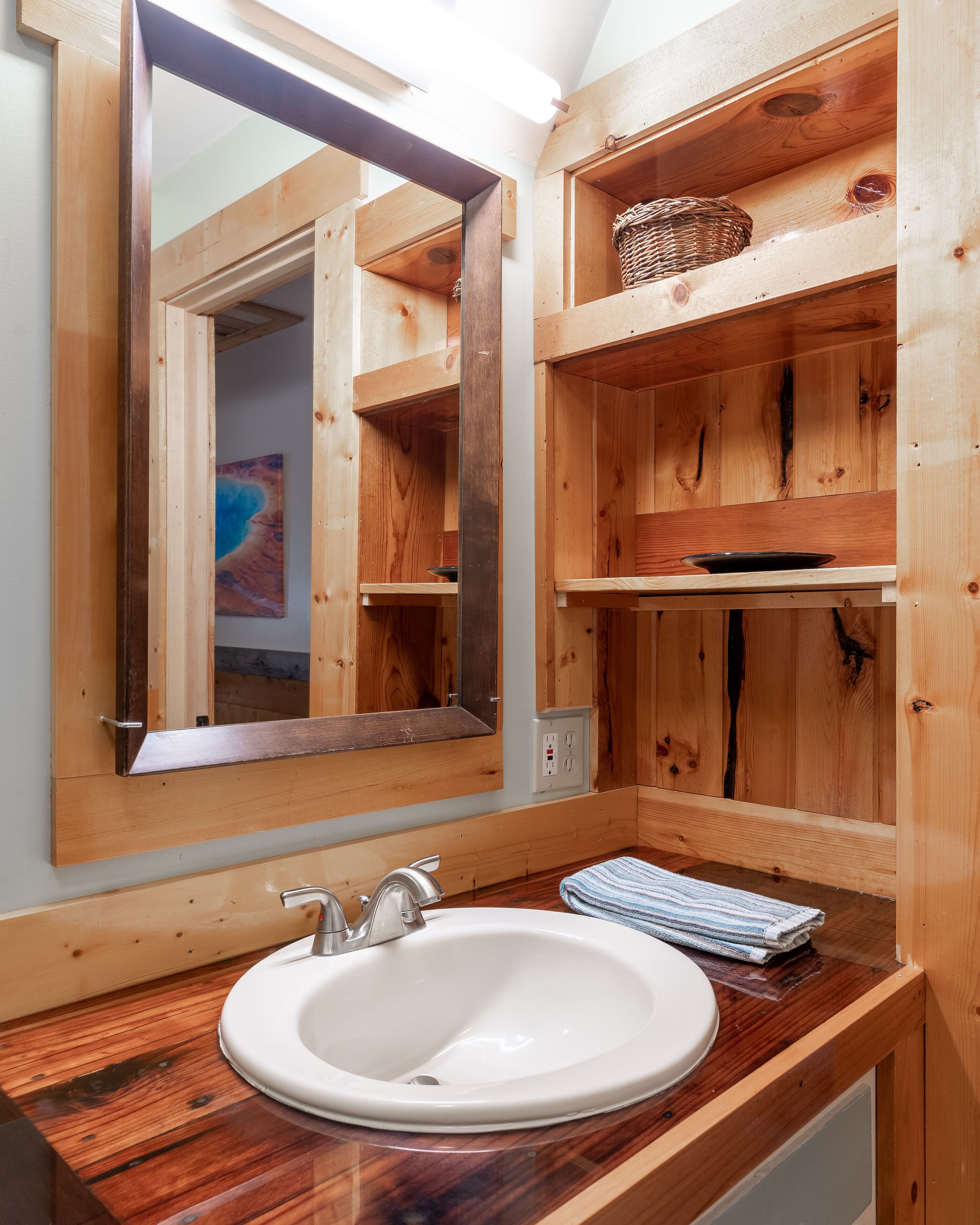 Une salle de bain en bois avec un grand miroir, un lavabo et des étagères.