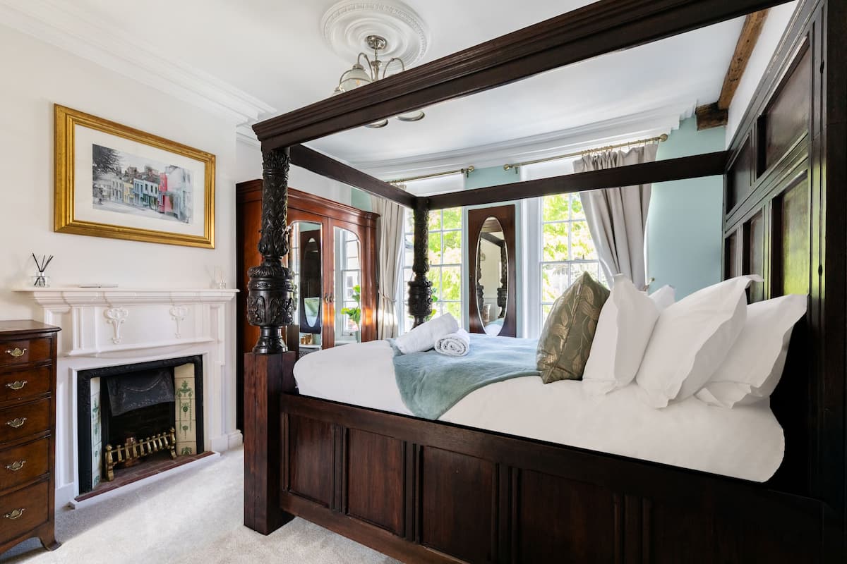 A bedroom with a four-poster bed, a fireplace, and a large window with curtains.