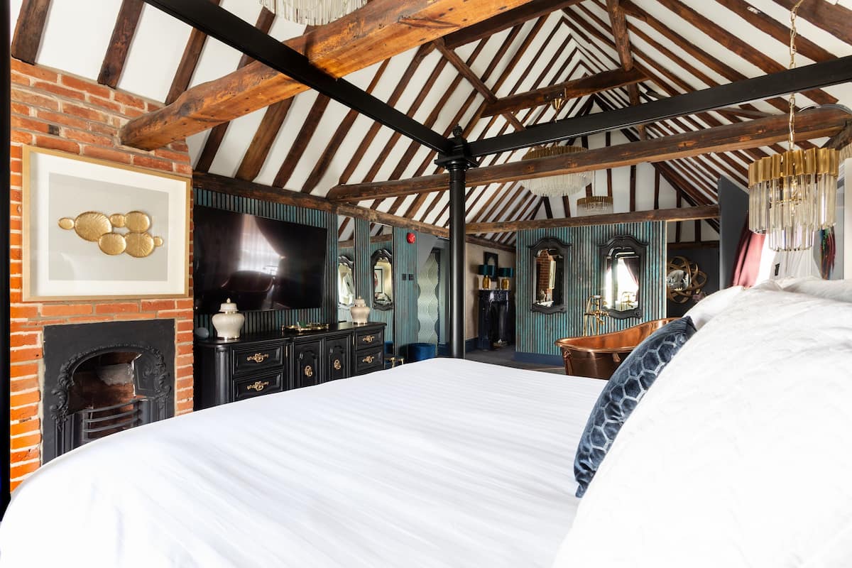 A bedroom with a large bed, a fireplace, a television, and a mirror.