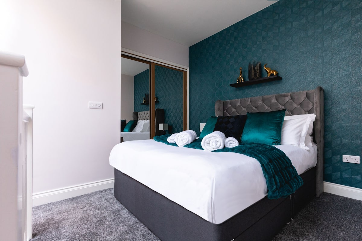 A bedroom with a bed, a mirror, a wall-mounted shelf with decorative items, and a door.
