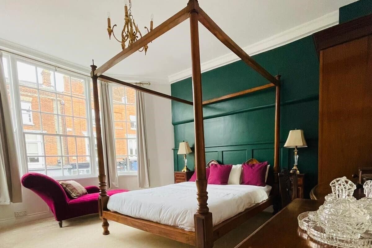 A four-poster bed with a wooden frame, a chaise lounge with a purple fabric, and a table with a crystal tray.