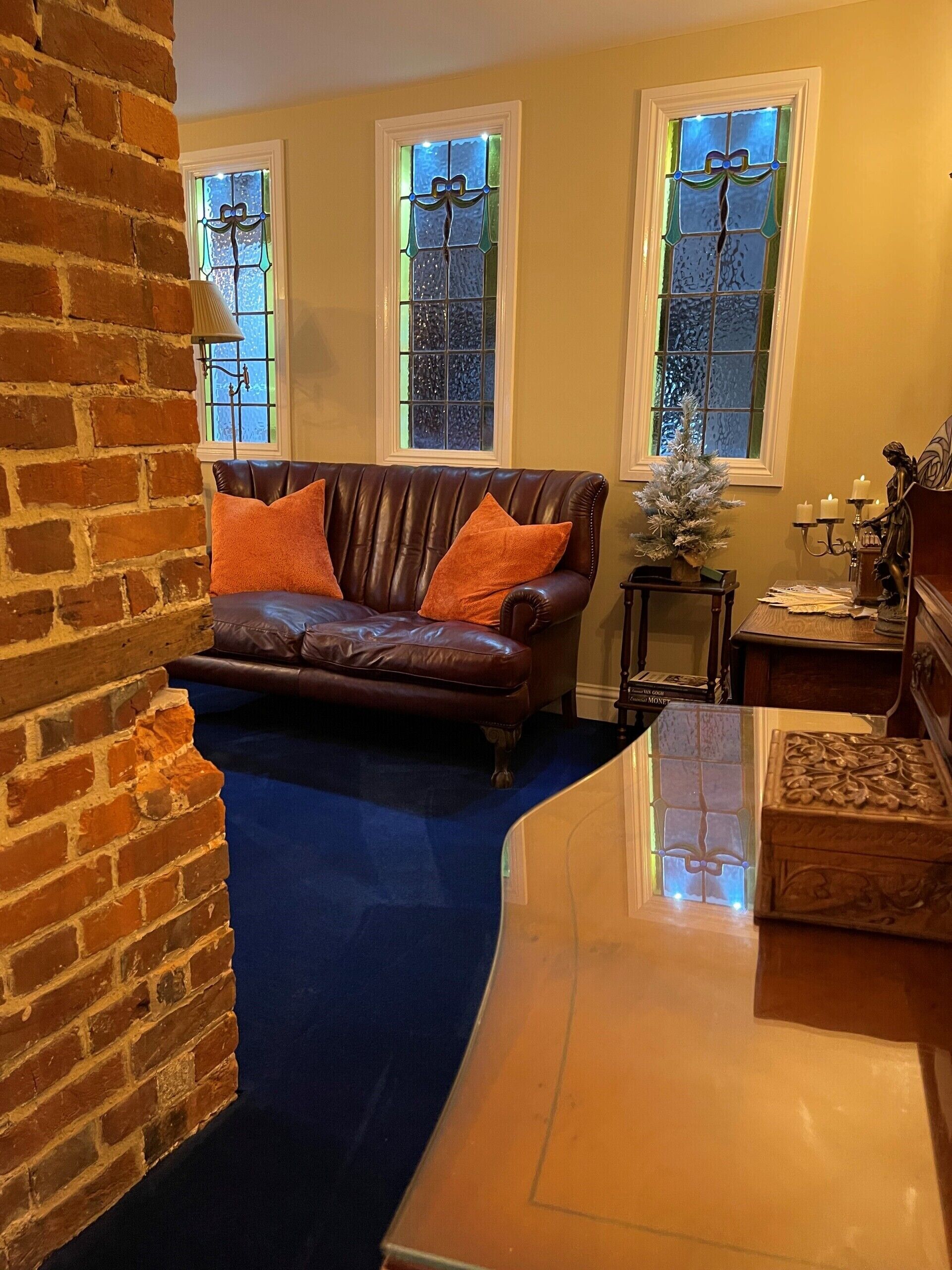 A living room with a brown leather sofa, orange cushions, a small Christmas tree, and a statue on a wooden table.