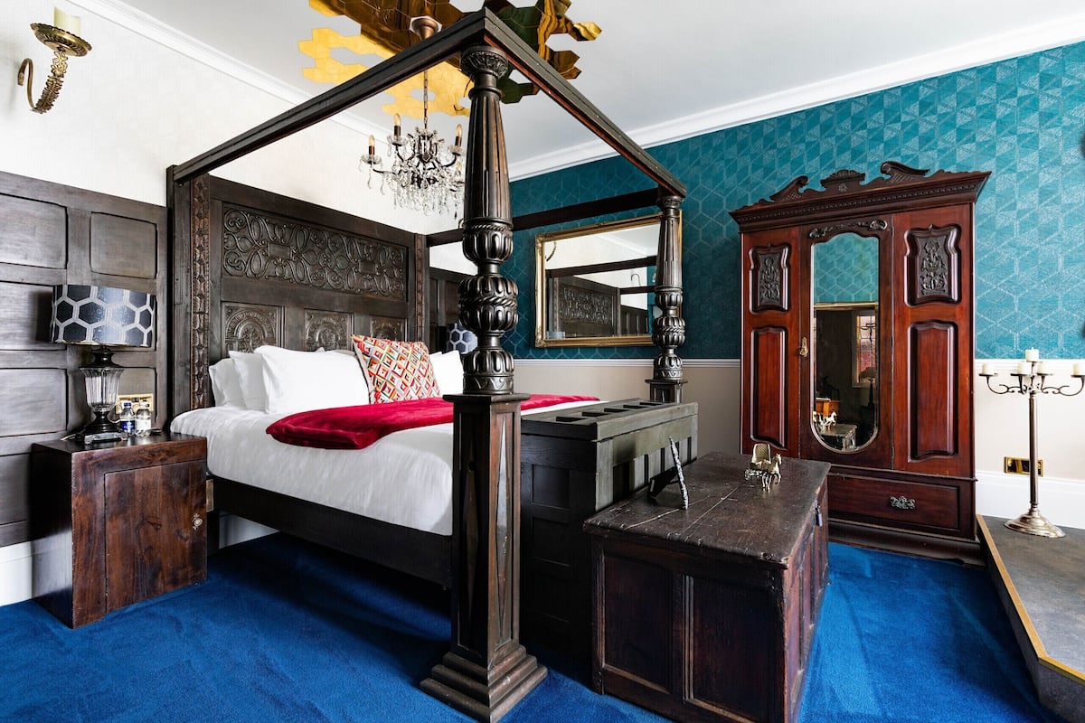 A four-poster bed with a canopy, a wooden nightstand, a dresser, and a large mirror.