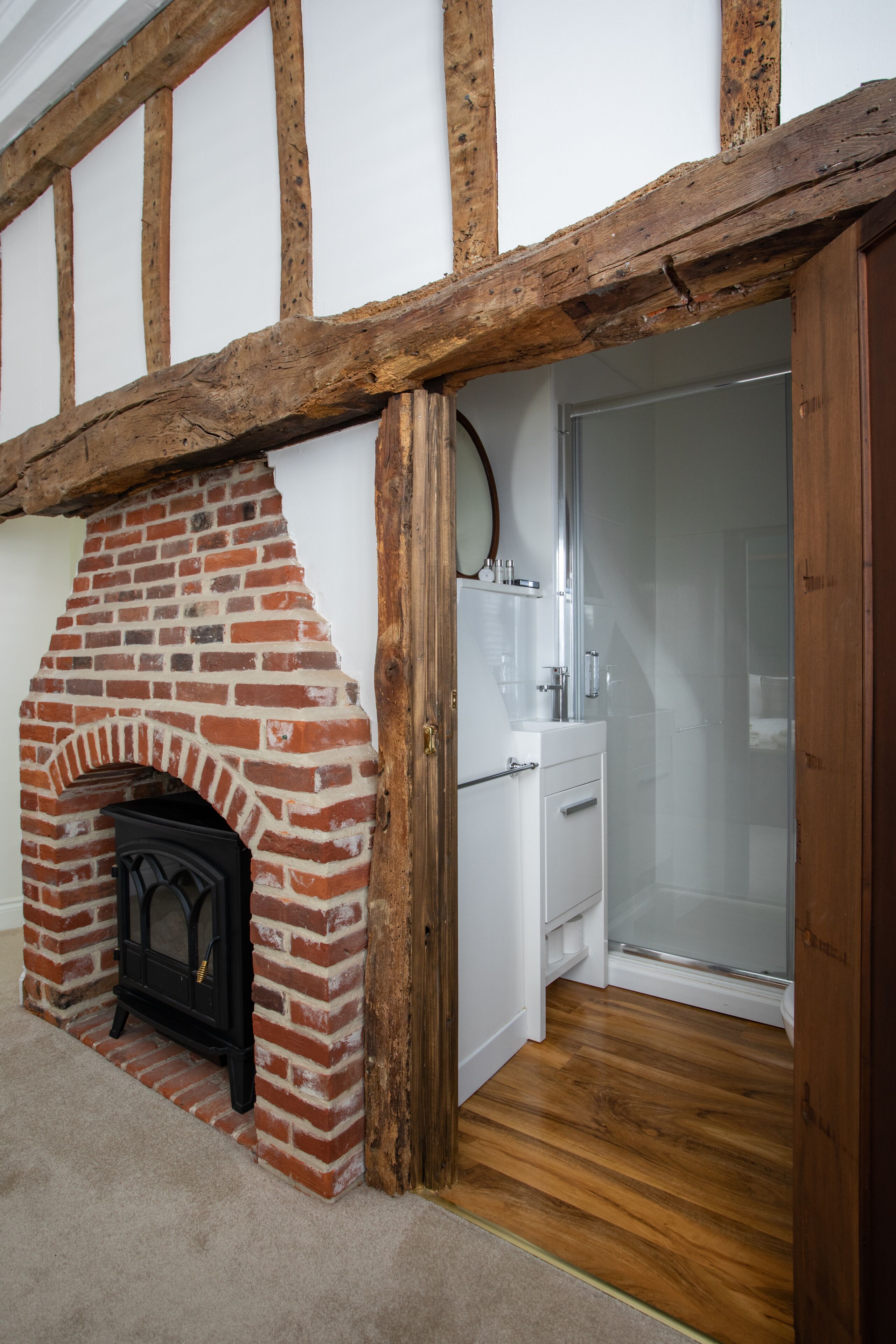 A room with a brick fireplace, wooden beams, a white sink, and a shower area.