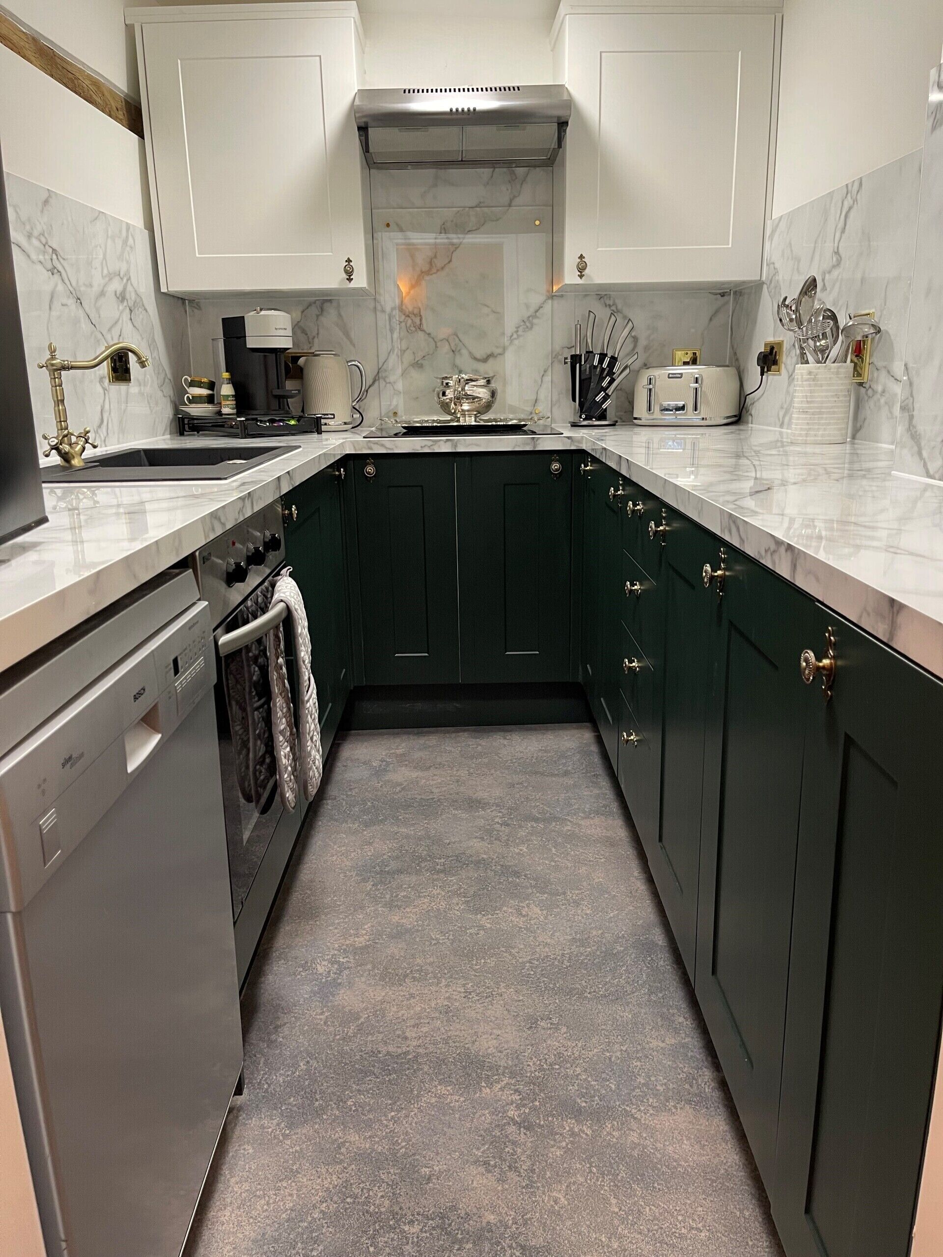 A modern kitchen with dark green cabinets, a white marble backsplash, and stainless steel appliances.