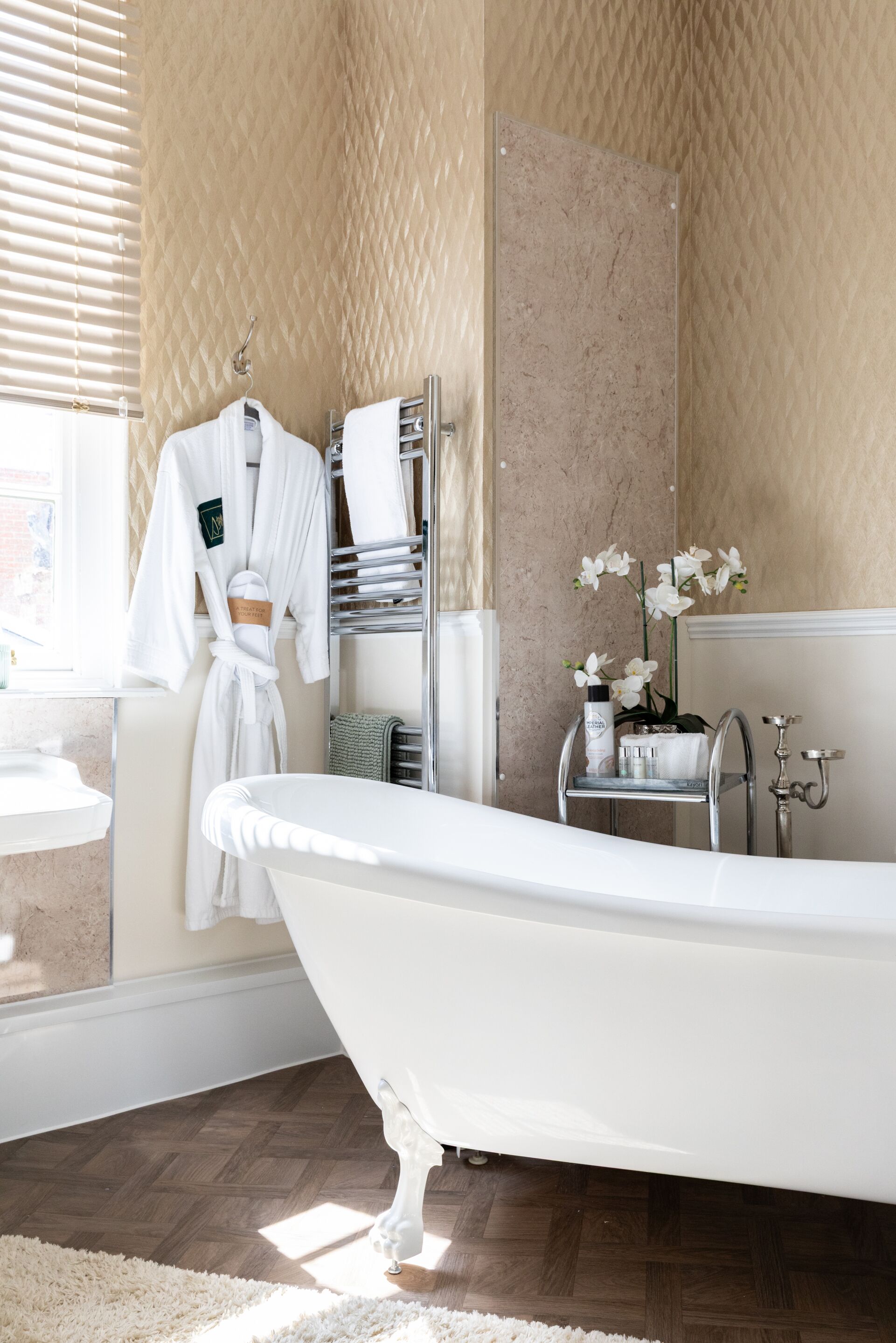 A bathroom with a freestanding bathtub, a towel rack with robes, a mirror, and a small shelf with toiletries.