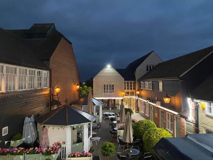Ein Innenhof mit Außenbestuhlung, einem Pavillon und einer Reihe von Gebäuden mit beleuchteten Fenstern.