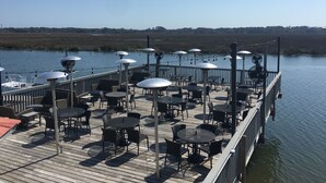 A deck with tables and chairs overlooking a body of water, with a railing and string lights. -  Poolside #, Westin Amenities Included with your stay.  #133 (Hilton Head Island)