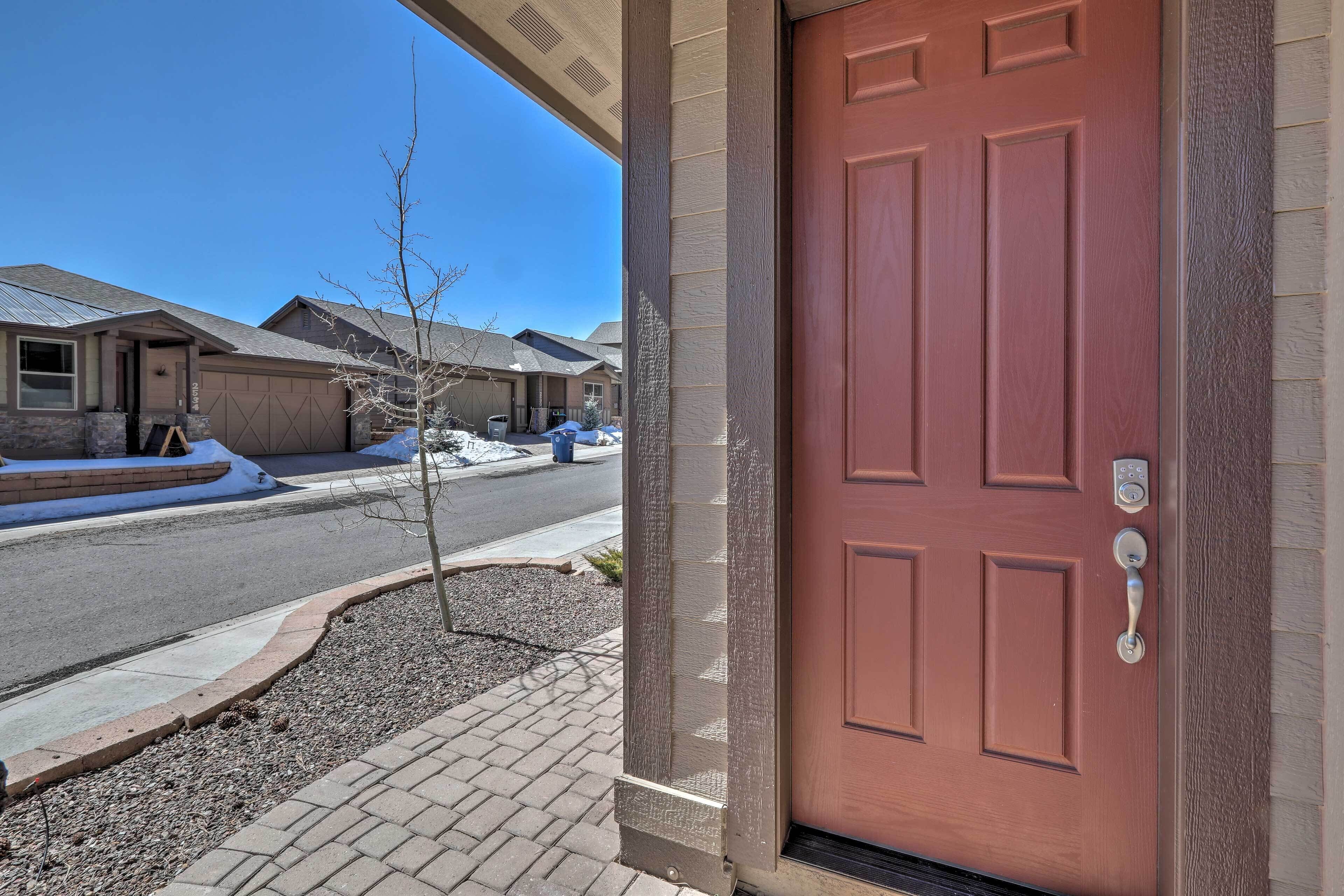 A residential entrance with a red door, a mailbox, and a small tree in the driveway.